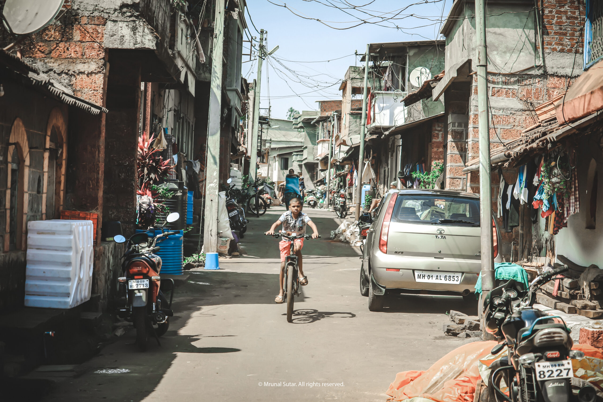 Candid photo of a boy cycling through a narrow Indian street with local shops, authentic street photography by LensVibrance